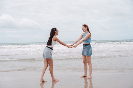Two young women holding hands and laughing playing on the beach, carefree friendship, freedom, and happiness. concept for summer fun, vacation, and joyful lifestyle.の写真素材
