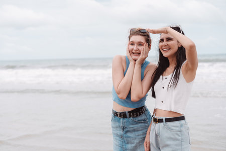 Two young women friends smiling and looking out at the ocean while standing on the beach. Perfect...