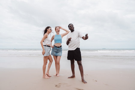 Diverse group of young friends taking selfie and enjoying time together on the beach. Fun summer vacation moment symbolizing friendship, freedom, and multicultural connection.の写真素材