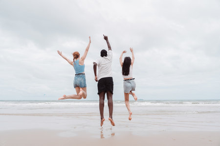 Happy diverse group of young people jumping on the beach, enjoying summer travel and friendship. Fun, freedom, and energy captured in a multicultural vacation moment.の写真素材
