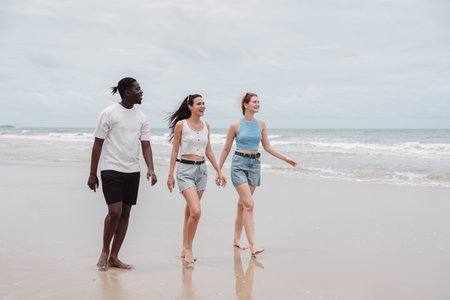 Diverse group of young friends walking on the beach together, smiling and enjoying summer vibes. Multicultural friendship and happy lifestyle on vacation.の写真素材