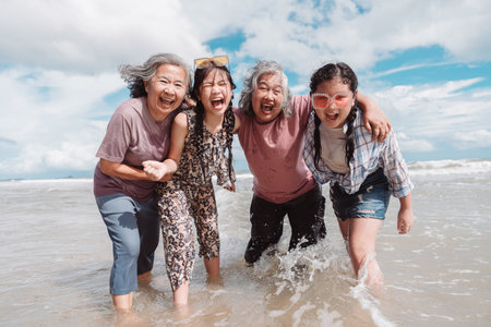 Happy Asian family generations laughing on the beach. elderly women, daughter, and a kid embracing joy, health and lifestyle.の写真素材