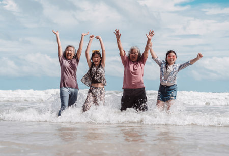 Asian multi generational family enjoying joyful moments on the beach. Happy women and daughter splashing water together, fun, bonding, and freedom across ages.の写真素材