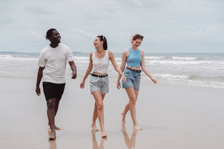 Diverse group of young friends walking on the beach together, smiling and enjoying summer vibes. Multicultural friendship and happy lifestyle on vacation.の写真素材