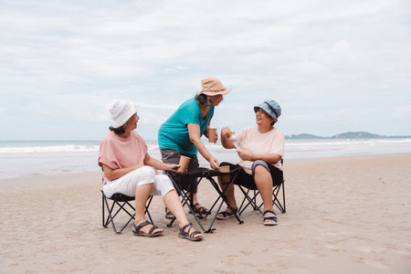 Asian senior females enjoying drinks together on the beach, retirement plans, friendship, and...