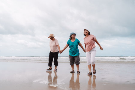 Senior women holding hands and walking joyfully along the beach shoreline. Concept of freedom, retirement lifestyle, and happiness in a natural coastal setting.の写真素材