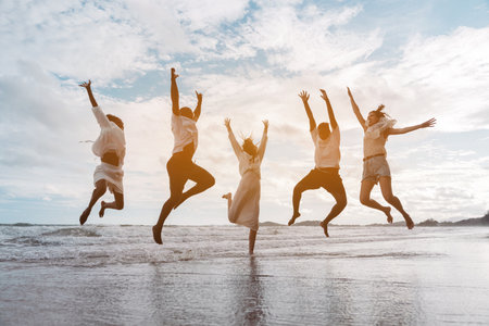 Diverse group of joyful friends jumping together on the beach with energy and excitement. freedom,...