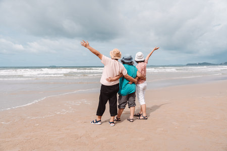Elderly women embracing and raising arms while enjoying a peaceful beach getaway. Concept of friendship, freedom, relaxation, and joyful retirement lifestyle.の写真素材