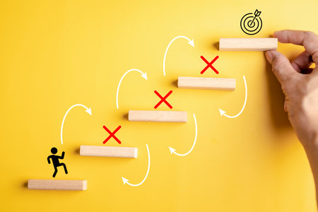 Step to success concept with wooden blocks, arrows, obstacles marked red crosses, and final target, challenges, problem solving, resilience, and achievement of goals.の写真素材