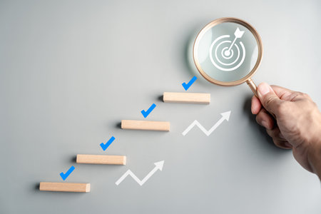 Planning and achievement with wooden blocks arranged as steps, check marks, magnifying glass with target icon, progress, goal setting, and business success.の写真素材
