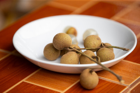 Longan fruit in a white plate on a brown wooden table.の写真素材