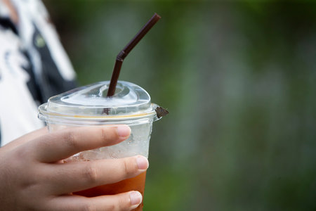 Iced coffee in plastic cup with straw in woman hand on nature background