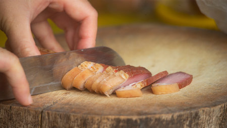 Chef slicing bacon with a knife on a wooden cutting board.