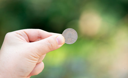 Hand holding coin on bokeh background, business and finance conceptの写真素材