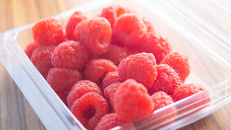 Raspberries in a plastic container on a wooden table. Selective focus.の写真素材