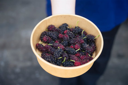 Mulberry in a bowl in the hands of a girl.