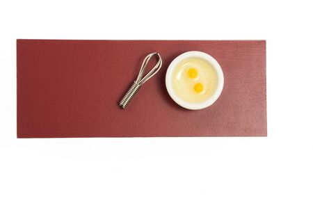 Two eggs in white bowl with whisk on red tableの写真素材