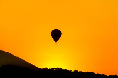 The rising sun in the morning and hot air ballon fly ovre mountain with Amazing yellow and orange colorの写真素材