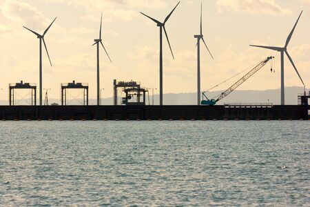 Silhouette of wind turbine and Heavy equipment on the ridge of the dam