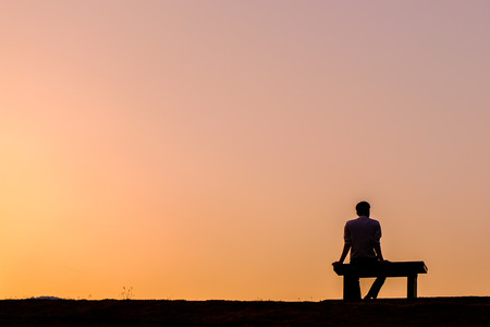 Silhouette man sitting on bench at golden hour, at Ang Kaew Reservoir, Chiang Mai University (Chiang Mai, Thailand)の写真素材