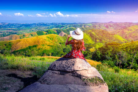 Asian girl wearing red dress sitting back hand catch white hat.view of phitsanulok province,Thailandの写真素材