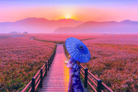 Bridge with woman in kimono with blue umbrella on background of mountains and sunriseの写真素材