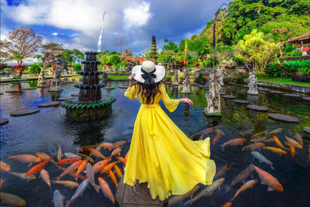 Woman wearing yellow dresses to feed koi fish in Taman Tirtagangga temple on Bali,Indonesiaの写真素材