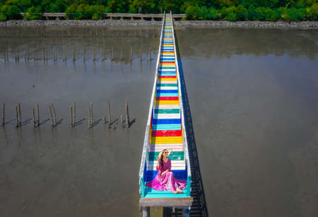 Asian women wearing purple dresses are sitting on the bridge at Rainbow Bridge, Kalong village, Samut Sakhon province, Thailandの写真素材