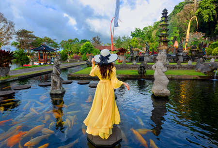 Woman wearing yellow dresses to feed koi fish in Taman Tirtagangga temple on Bali,Indonesiaの写真素材