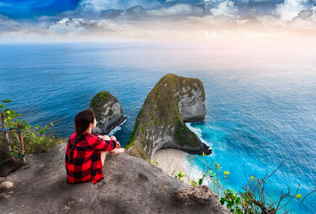 Girl sitting on a cliff and enjoys the view to trex mountain on nusa penida island in bali ,Indonesiaの写真素材