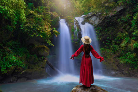Rear view of young woman standing in front of waterfall with her hands raised at Sapan Waterfall, Khun Nan National Park, Boklua District, Nan Province, Thailandの写真素材