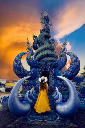 Asian tourists stand to admire a blue statue in a temple in Chiang Rai, Thailandの写真素材
