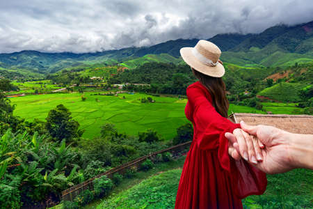 Asian woman wearing a white hat and a red dress stands to admire the beauty of Ban Sa Pan rice fields in Nan Province, Thailandの写真素材
