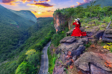 Thai woman in red dress sitting on the rock at Pha luang daeng viewpoint, Chiang mai, Thailandの写真素材