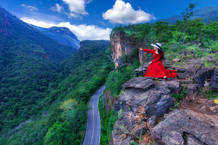 Thai woman in red dress sitting on the rock at Pha luang daeng viewpoint, Chiang mai, Thailand.の写真素材