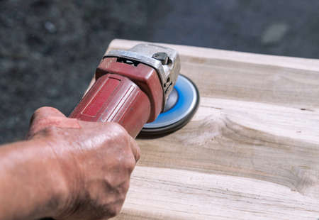 A carpenter worker is grinding a wooden surface with an electric sander