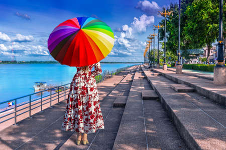 Thai woman holding a rainbow umbrella stands on the banks of the Mekong River in Nakhon Phanom Province, Thailandの写真素材