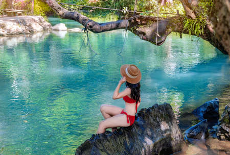 Asian woman in swimsuit sitting on a rock In the Blue Lagoon near Vang Vieng, Laosの写真素材