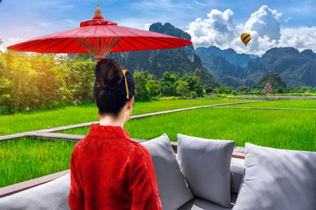 Asian woman holding umbrella looking at wooden walkway with green rice fields in Vang Vieng, Laosの写真素材