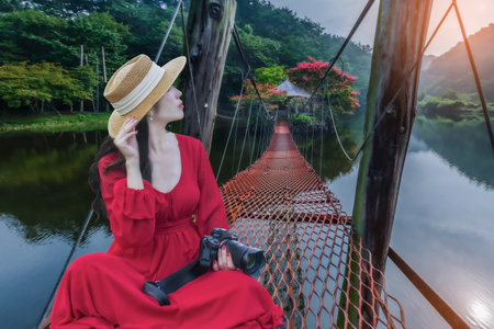 Asian woman sits on a red bridge leading to an island in the middle of the water with colorful flowersの写真素材