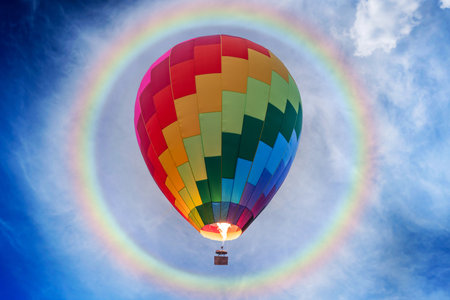 Colorful balloons soar in the sky with many flames and huge rainbow halo at noonの写真素材
