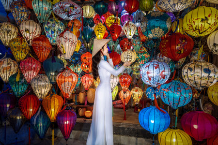 Asian woman wearing Ao Dai Vietnamese dress with colorful lanterns, traveler sightseeing at Hoi An ancient town in central Vietnamの写真素材