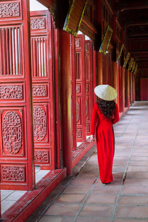 A young tourist in ao dai looks at the adjustable gate of the ancient palace of the Imperial Citadel...