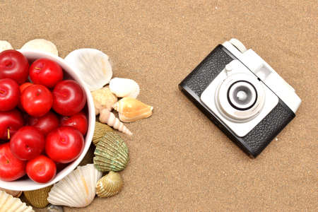 Red plums, old camera, shells and white hat on sand