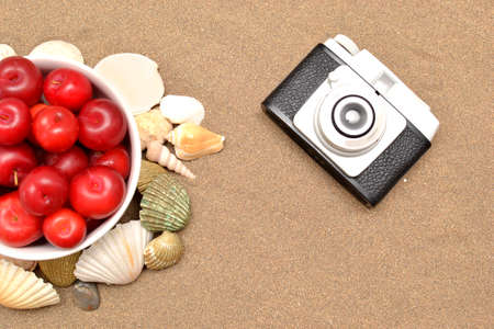Red plums, old camera, shells and white hat on sandの写真素材
