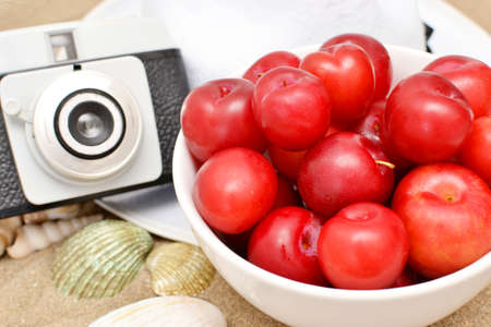 Red plums, old camera, shells and white hat on sandの写真素材