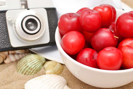 Red plums, old camera, shells and white hat on sandの写真素材