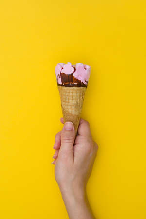 Hand holding ice cream cone on yellow backgroundの写真素材