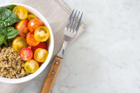 Quinoa salad in bowl with tomatoes and spinach on marble tableの写真素材