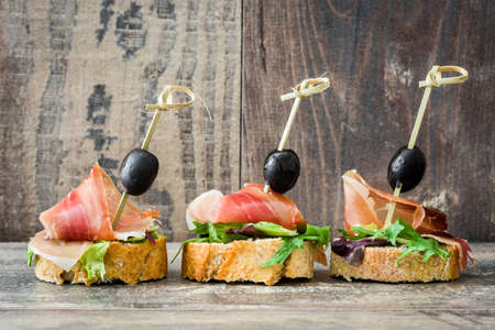 Spanish serrano ham skewers with olives and lettuce on a rustic wooden backgroundの写真素材